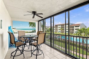 A balcony with a table and chairs, a ceiling fan, and a view of a beach and pool.