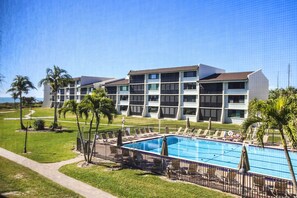 A hotel with a swimming pool, palm trees, and a clear blue sky. - Loggerhead Cay 562 - Partial gulf view, beach side vacation rental condo (Sanibel)