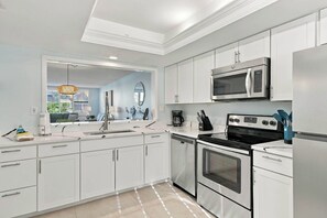A modern kitchen with white cabinetry, a stainless steel refrigerator, a microwave, an oven, and a dishwasher.