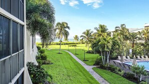 A well-maintained lawn with a pathway, palm trees, and a pool area. - Loggerhead Cay 562 - Partial gulf view, beach side vacation rental condo (Sanibel)
