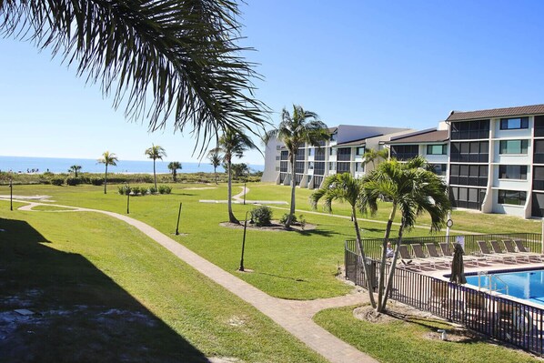 A resort with a swimming pool, palm trees, and a view of the ocean. - Loggerhead Cay 562 - Partial gulf view, beach side vacation rental condo (Sanibel)