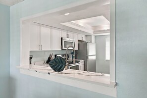 A modern kitchen with white cabinetry, a stainless steel refrigerator, and a microwave. - Loggerhead Cay 562 - Partial gulf view, beach side vacation rental condo (Sanibel)