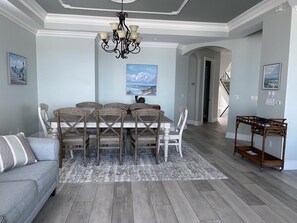 A dining area with a wooden table and chairs, a chandelier, and artwork on the walls. - Beachfront LUXURY HOME- Watch the waves from your pool & 15 steps to the beach (Ft. Myers Beach)