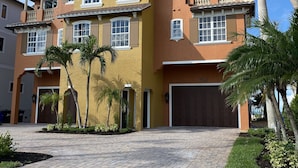 A multi-story residential building with a brick driveway, palm trees, and a garage.
