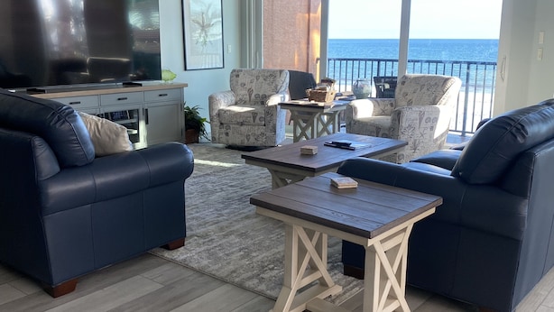 A spacious living room with a large TV, two sofas, a coffee table, and a balcony with a view of the ocean.