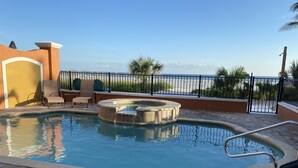 A swimming pool with a hot tub, lounge chairs, and a view of the beach.