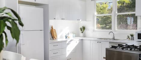 A modern kitchen with white cabinetry, a gas stove, and a window with a view of greenery.