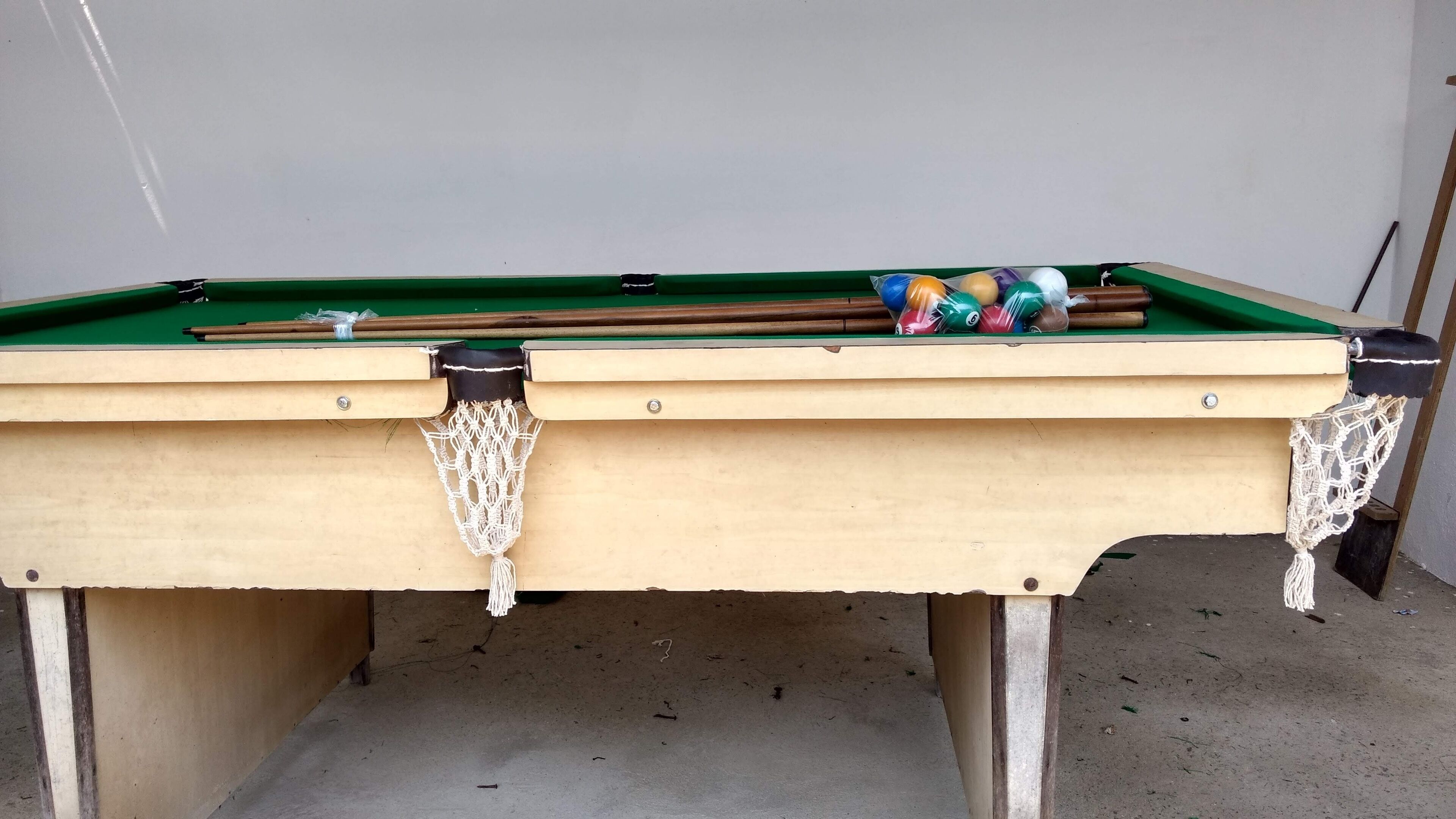 A pool table with a green felt surface, surrounded by a beige frame with decorative netting.