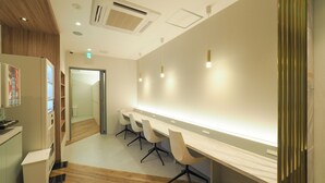 A modern conference room with a long table, white chairs, and a vending machine. - LEO YU CAPSULE HOTEL Funabashi (Funabashi)