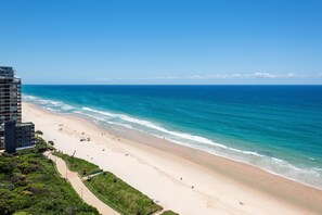 A beach with a clear view of the ocean, a sandy shore, and a building with multiple floors.
