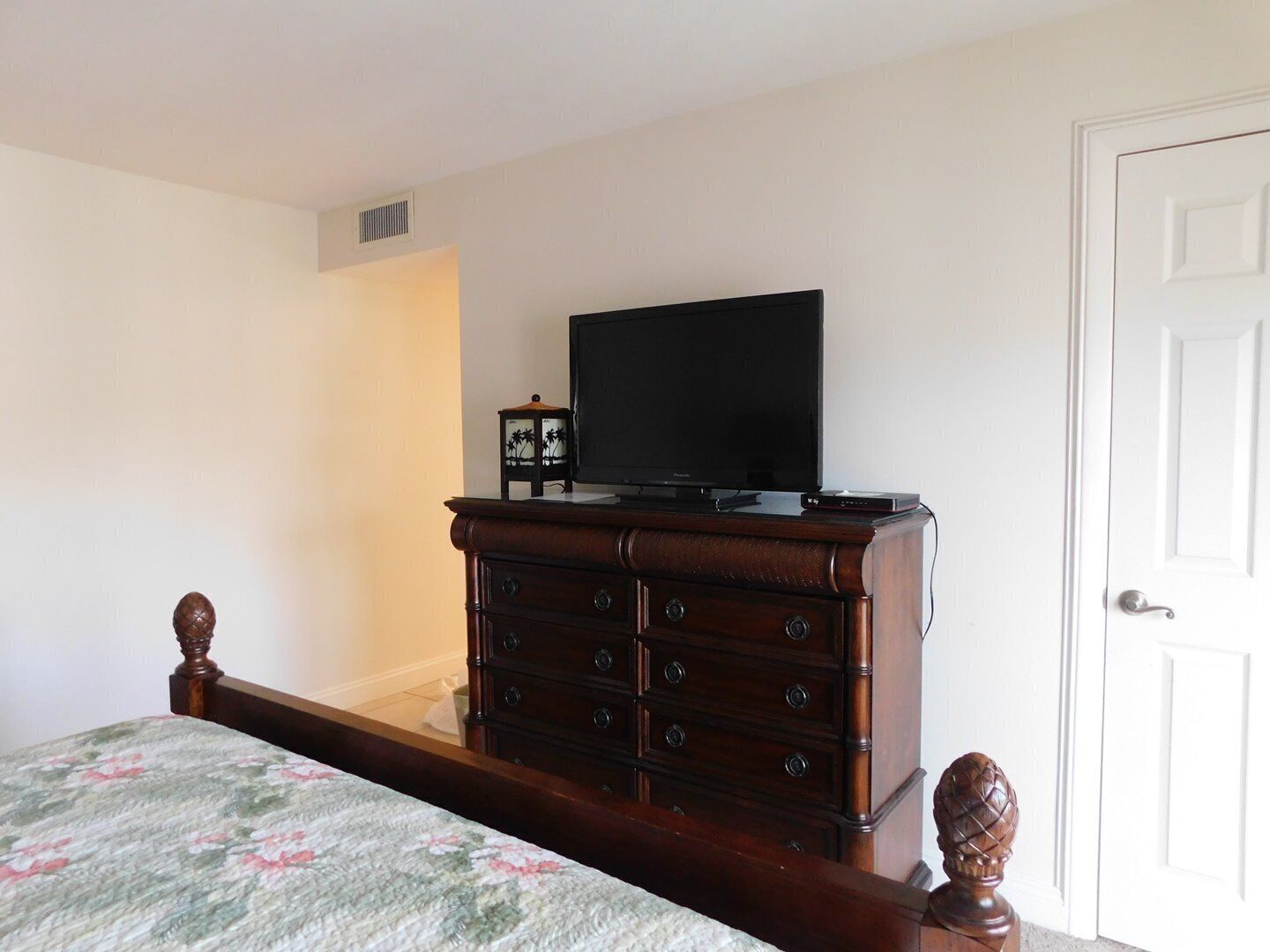 A bedroom with a bed, a dresser with a television, and a door.