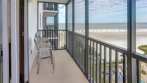 A balcony with a view of the beach, a small table, and a chair.