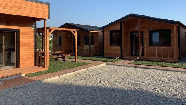 A row of wooden cabins with a gravel driveway and a picnic table in the center. - Recinto Hotelero As Casiñas (Cangas)