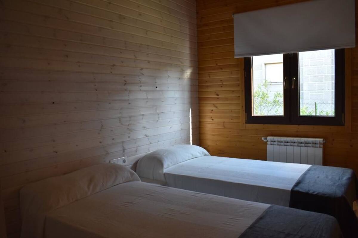 Quarto com duas camas, paredes de madeira, uma janela e um radiador.