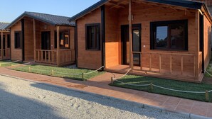 A row of wooden cabins with a porch, a gravel driveway, and a grassy area. - Recinto Hotelero As Casiñas (Cangas)