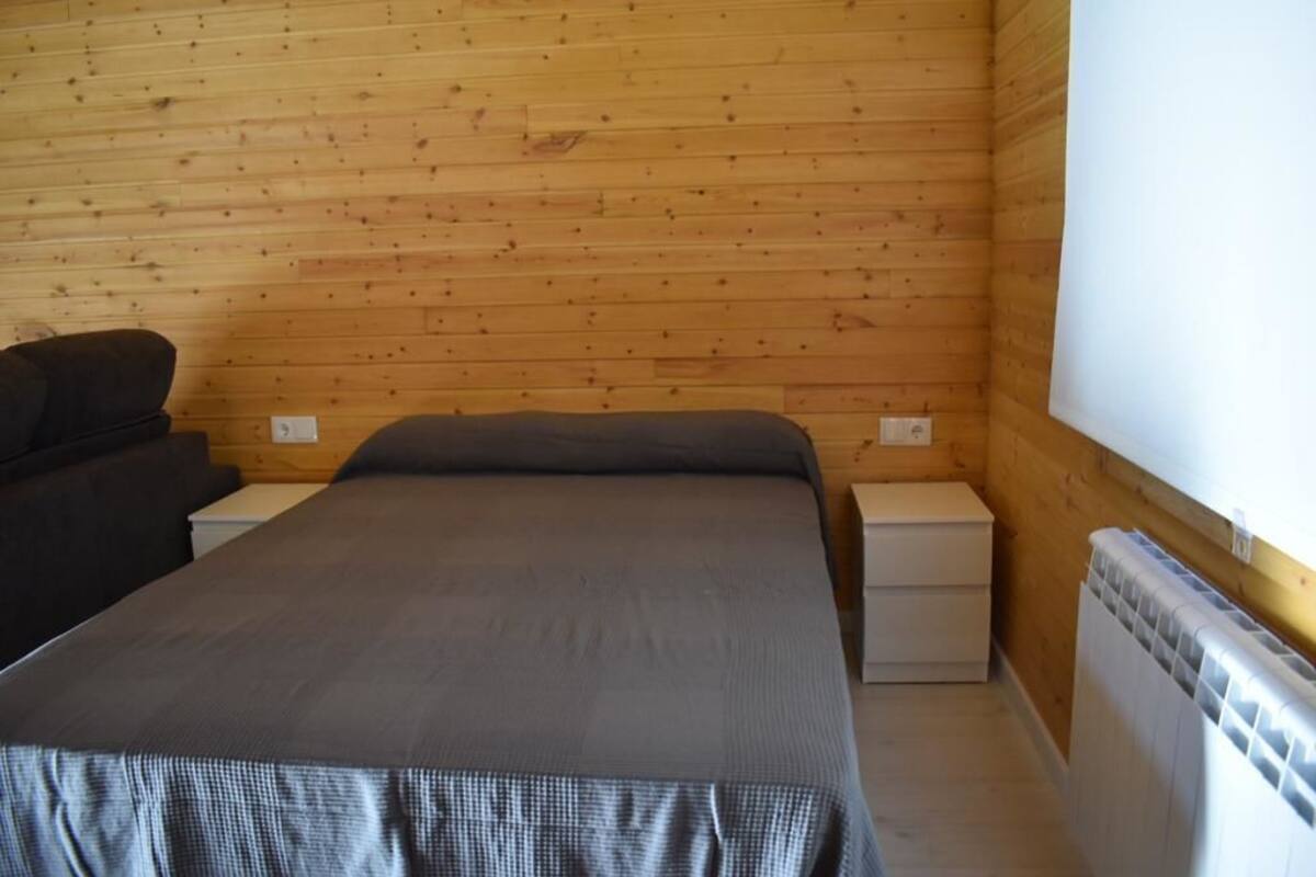 Uma cama de solteiro com um cobertor cinzento num quarto com paredes de madeira e um radiador branco.