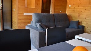 A modern log cabin interior with a grey sofa, a white table, and a laptop on the table. - Recinto Hotelero As Casiñas (Cangas)