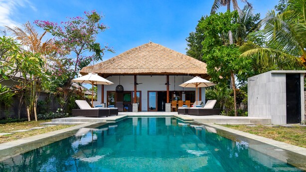 A modern house with a pool, two umbrellas, and lounge chairs.