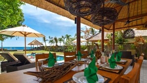A dining area with wooden tables, green napkins, and thatched umbrellas.
