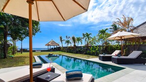 A poolside area with lounge chairs, a table with a drink, and a view of the ocean.