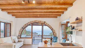 Ein modernes Interieur mit einem Fenster mit Steinbogen, einer Couch, einem Essbereich und einer Küche mit Spüle und Regalen.