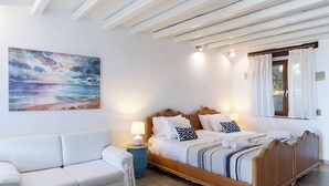 Ein Schlafzimmer mit einem hölzernen Bett, weißer Bettwäsche, einem blauen Nachttisch, einer weißen Couch und einem Bild von einer Strandansicht.