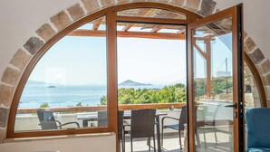 Ein Zimmer mit einem großen Bogenfenster und Blick auf das Meer und grüne Landschaft.