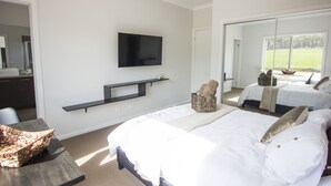 A modern hotel room with a large bed, a TV mounted on the wall, a small seating area, and a view of the outdoors. - Fully furnished 2 room apartment - sleeps 4 (Axedale)