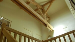 Une pièce avec des poutres apparentes, un escalier avec des rampes en bois et une porte ornée d’un miroir décoratif.