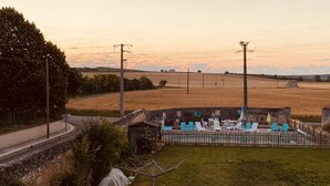 Un espace extérieur aménagé dans un cadre rural, avec des chaises et une table, entouré d’une clôture en bois et d’un mur en pierre.