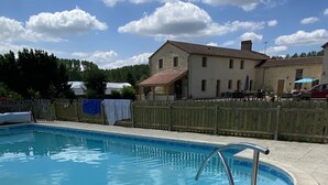 Une piscine avec une terrasse carrelée, une clôture en bois et un bâtiment en arrière-plan.