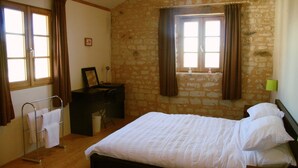 Une chambre avec un mur en pierre, un lit, un bureau et une fenêtre avec des rideaux.