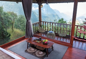 Un balcón con mesa de madera, sillas de mimbre y vista a las montañas.