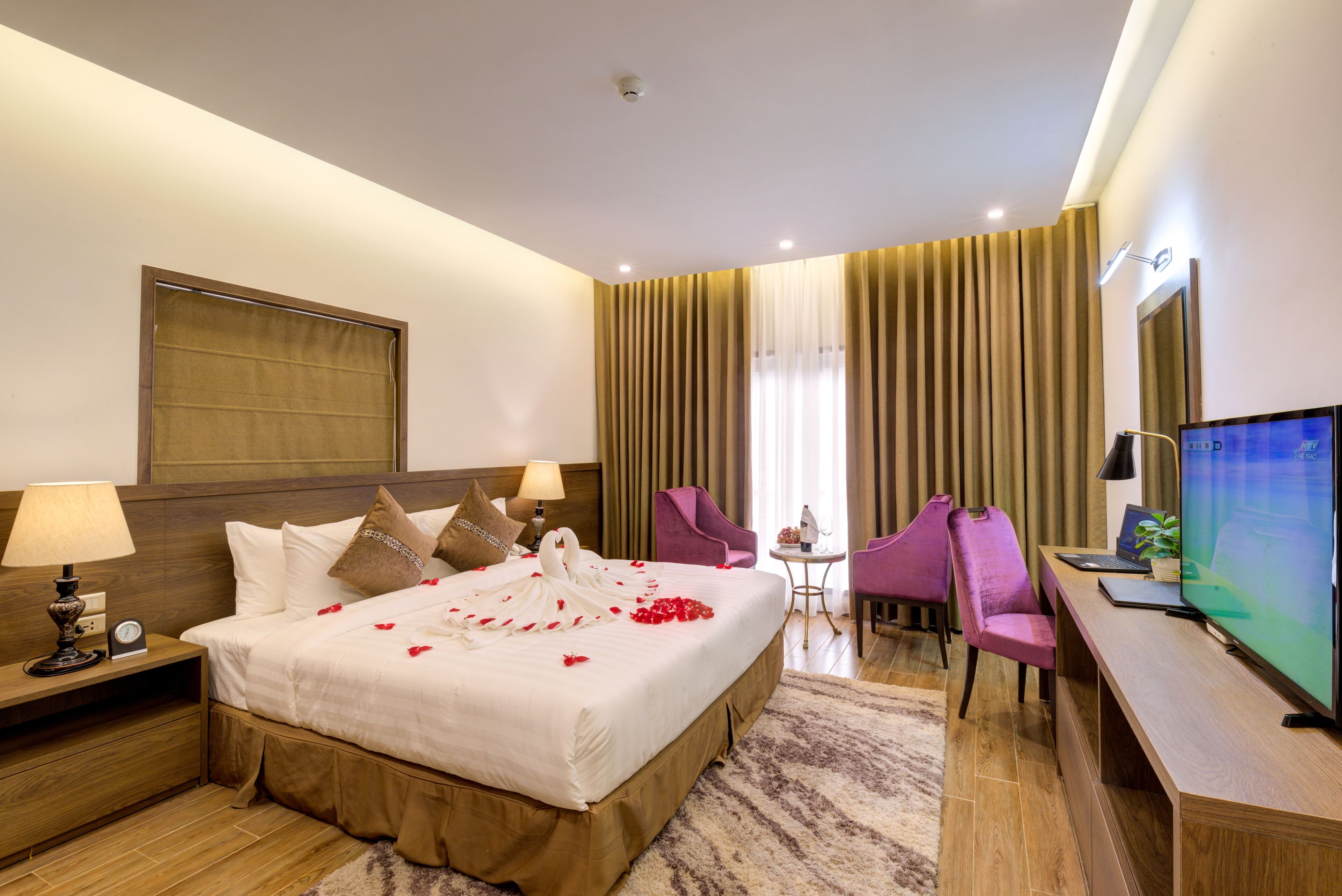 A hotel room with a large bed, a desk, a chair, a TV, and a window with curtains.