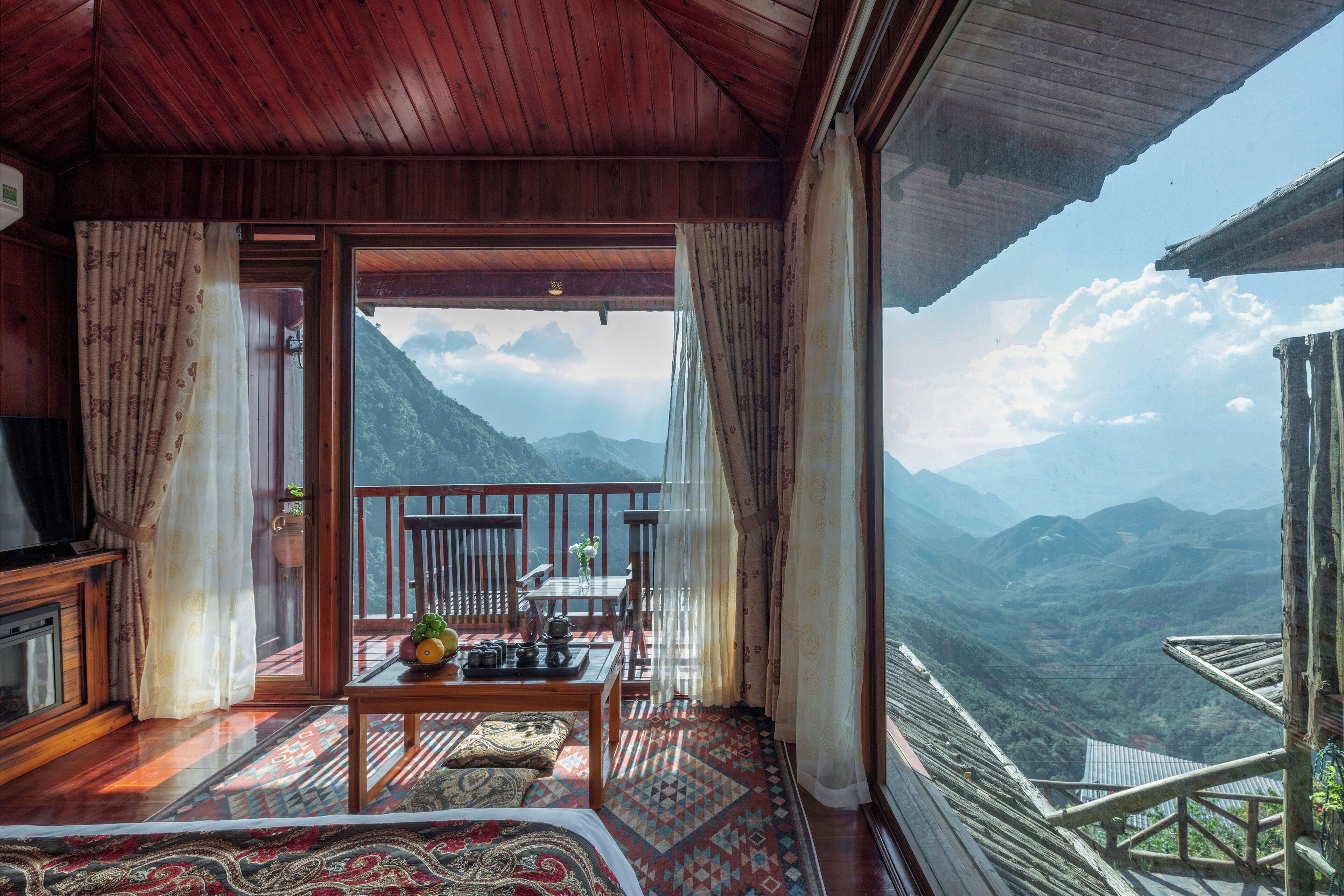 A room with a balcony, a wooden ceiling, and a view of mountains.