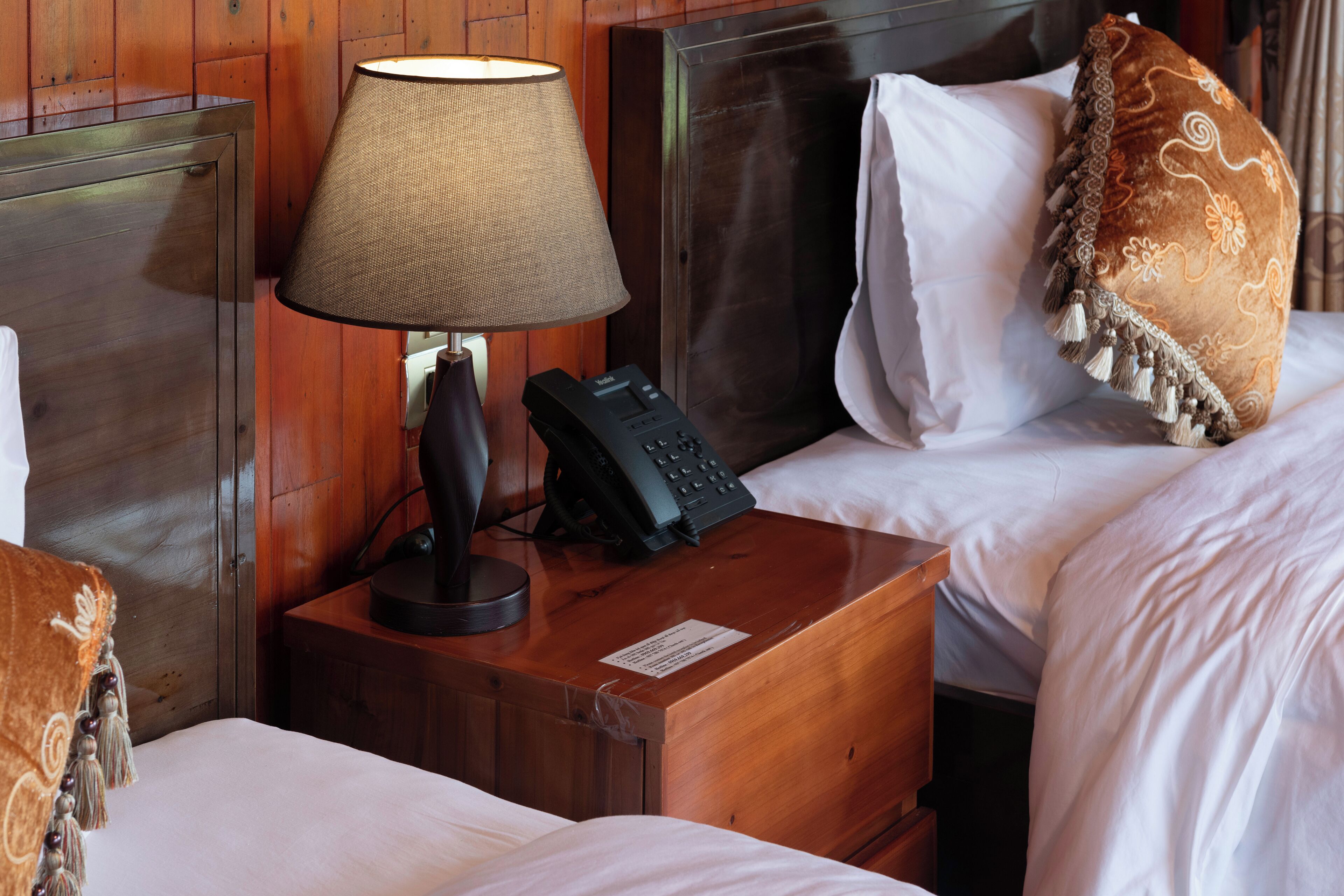 A hotel room with a wooden headboard, a bedside lamp, a telephone, and a decorative pillow.