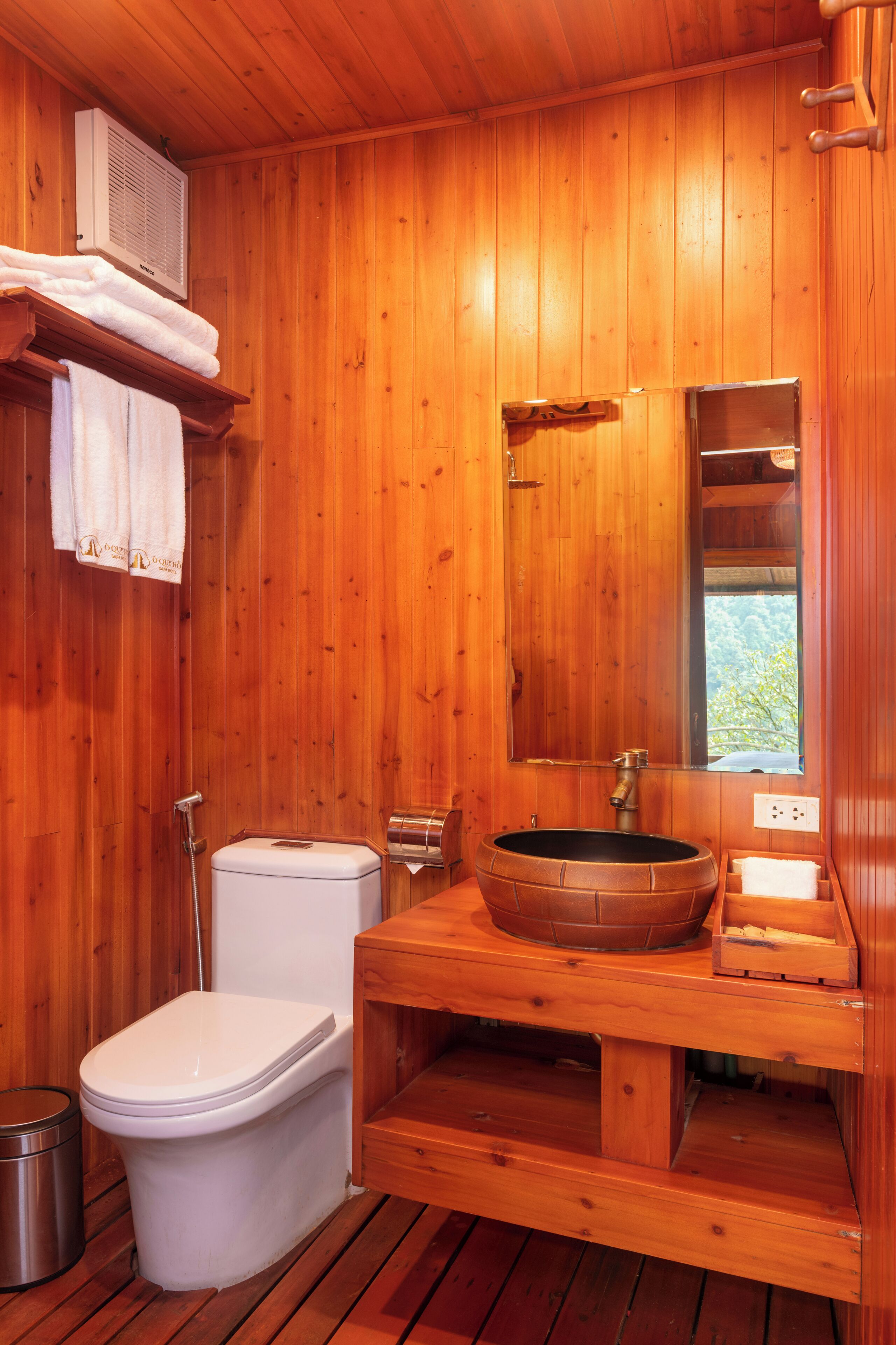 A wooden cabin-style bathroom with a toilet, sink, and shower.