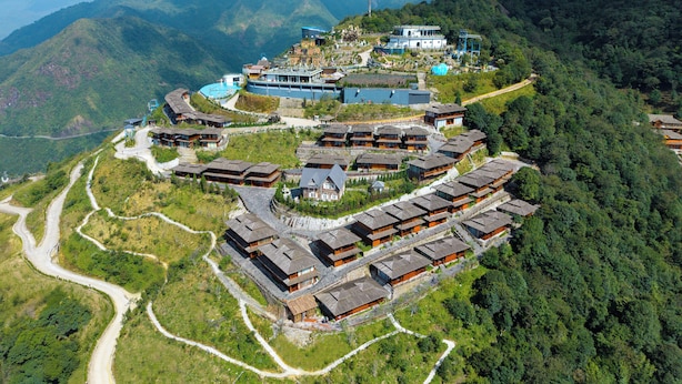 A hillside resort with traditional wooden buildings, a swimming pool, and a winding road.