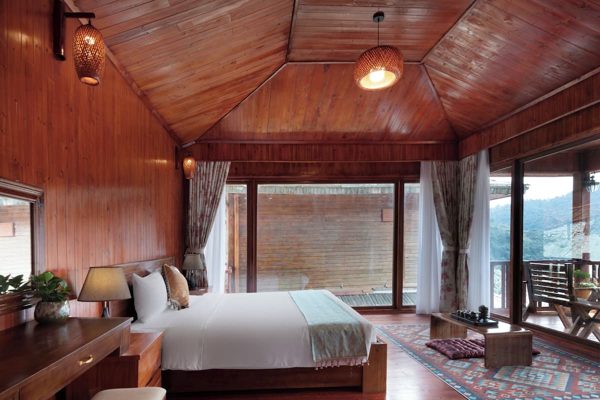 A wooden bedroom with a bed, bedside tables, a desk, and a balcony with a view.