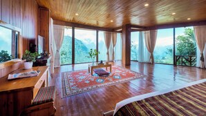 A spacious room with wooden floors, large windows, a wooden ceiling, and a view of mountains.