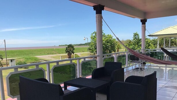 Un espacio de estar al aire libre techado con mobiliario de ratán negro, una hamaca y vistas a un paisaje verde y el horizonte distante.