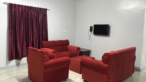 Una sala de estar con un sofá rojo, un televisor de pantalla plana montado en la pared y un ventanal con cortina.