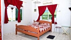 Un dormitorio con cama de madera, cortinas rojas, una mesita y una silla.