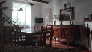 Una zona de menjador amb taula i cadires de fusta, televisió, làmpada i un quadre a la paret.