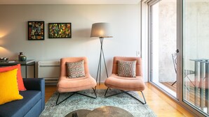 A modern living room with two pink armchairs, a blue sofa, and a floor lamp. There are two abstract paintings on the wall and a large window providing natural light. - Porto Insight Apartment Cedofeita- Balcony & Parking (Porto)