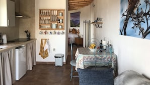 Eine gemütliche Küche mit Holzbalken, ein Essbereich mit Tisch für zwei Personen und ein Schlafzimmer mit Bett und Nachttisch.