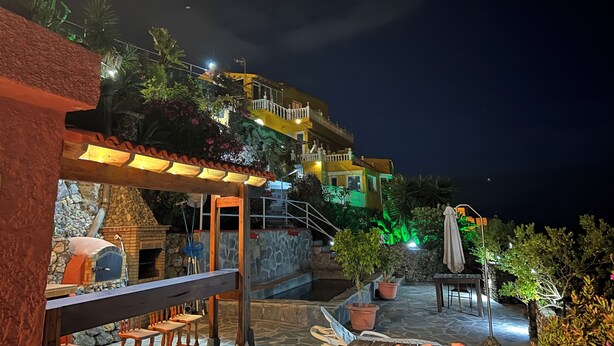 Ein Hotel bei Nacht mit Außenbestuhlung, einem Steinkamin und einer Treppe, die zu einem Balkon führt.
