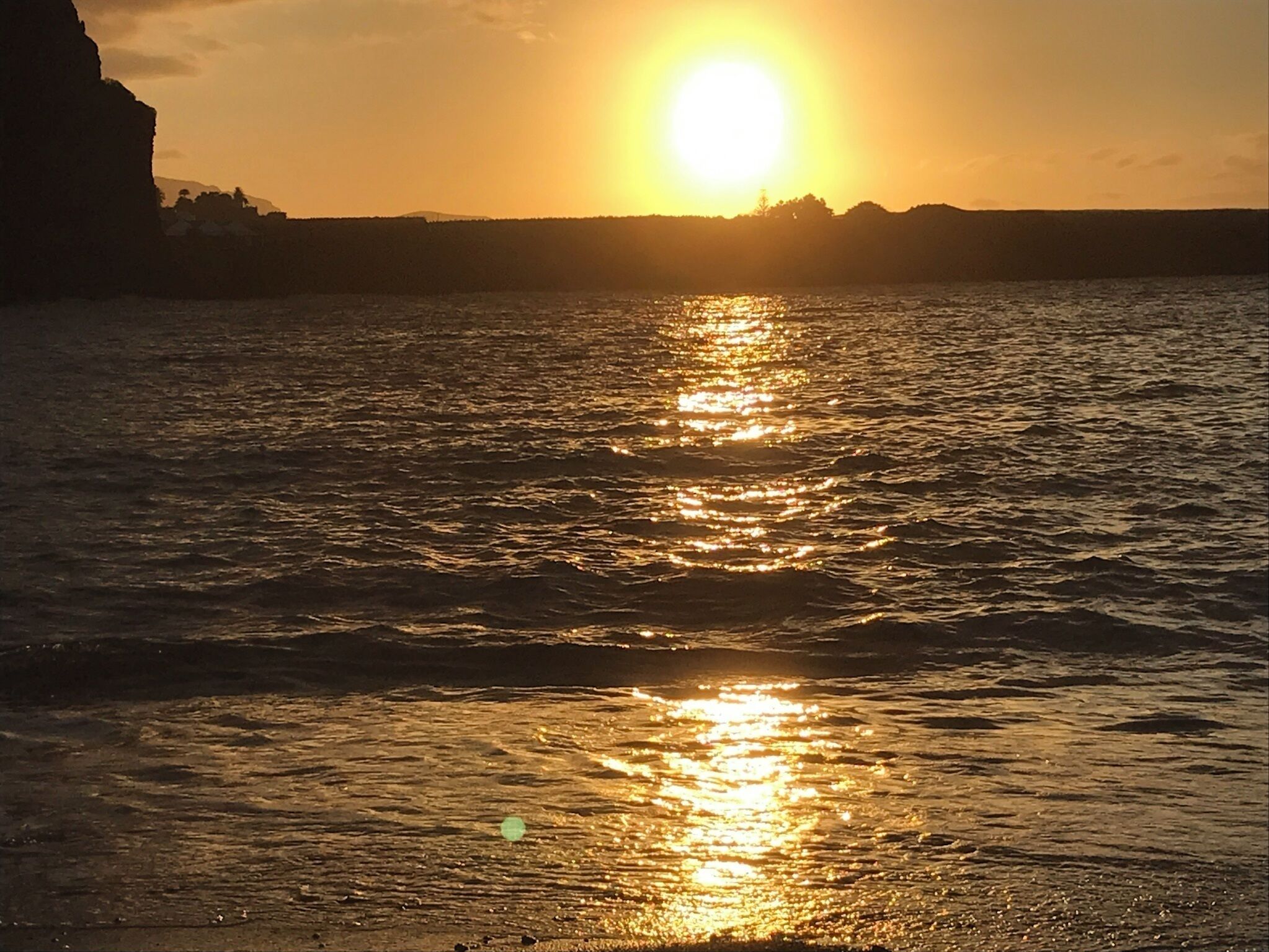 Un coucher de soleil sur une étendue d’eau, avec la silhouette d’une falaise et d’une terre lointaine.