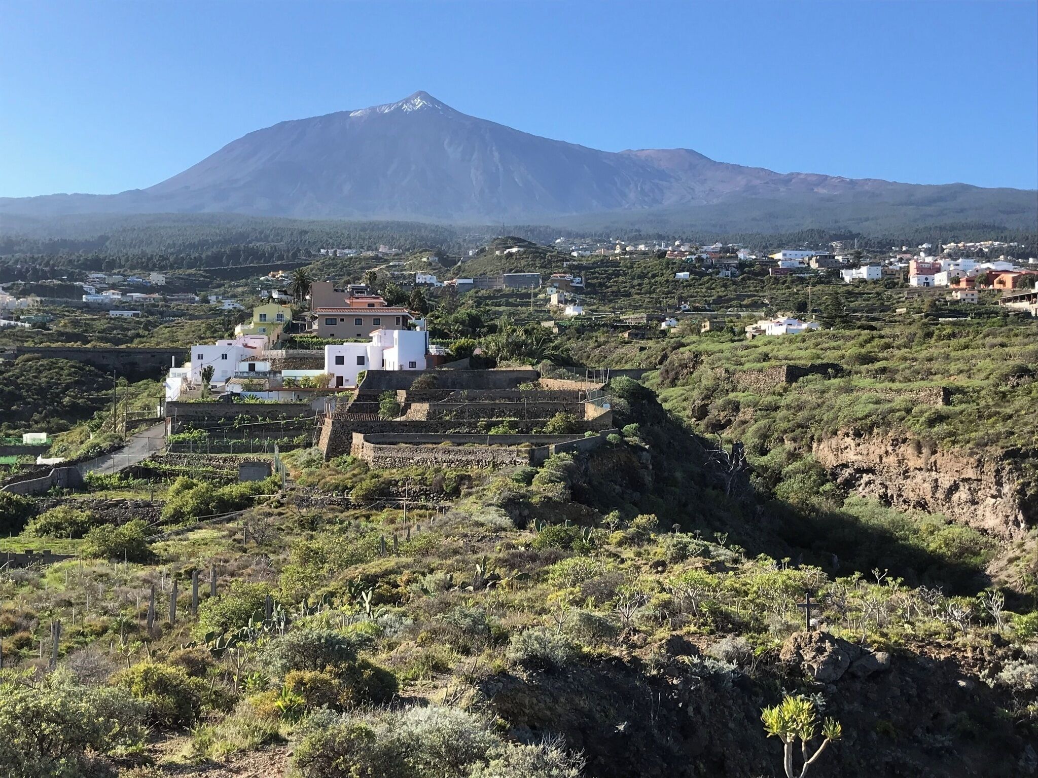 Un pueblo con edificaciones en una ladera, una montaña al fondo y vegetación escasa.