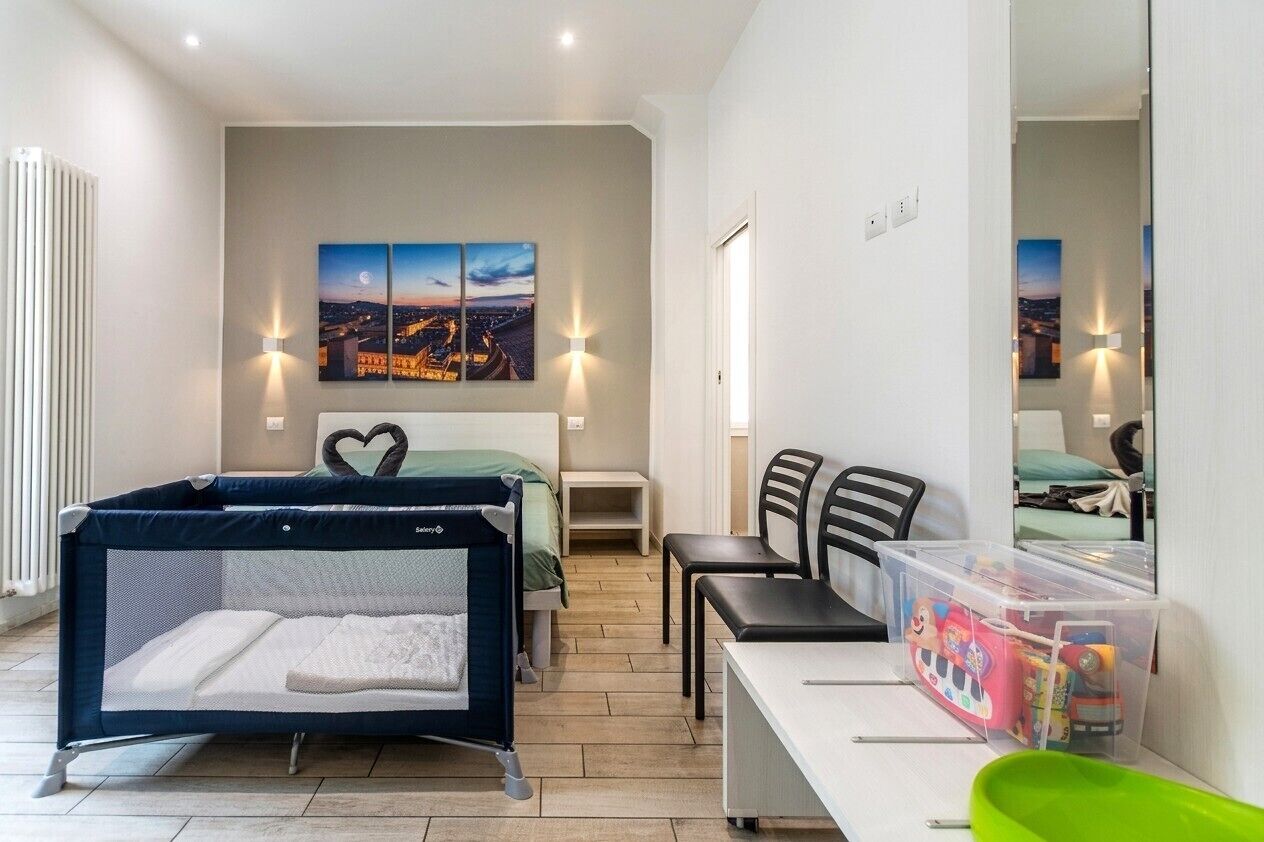 A bedroom with a bed, a desk, a chair, a crib, and a wall-mounted TV.